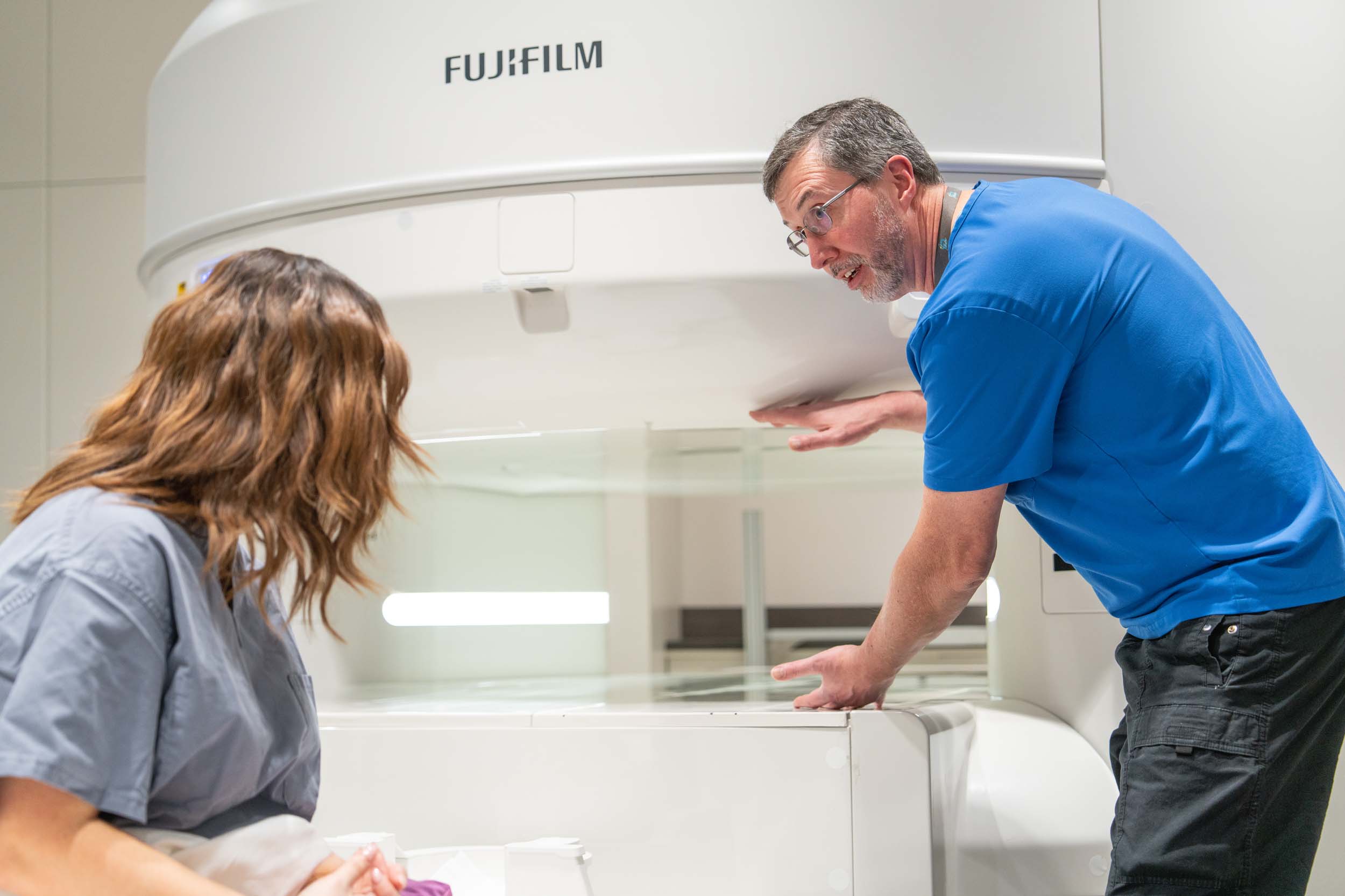 A technical explains the open MRI machine to a patient