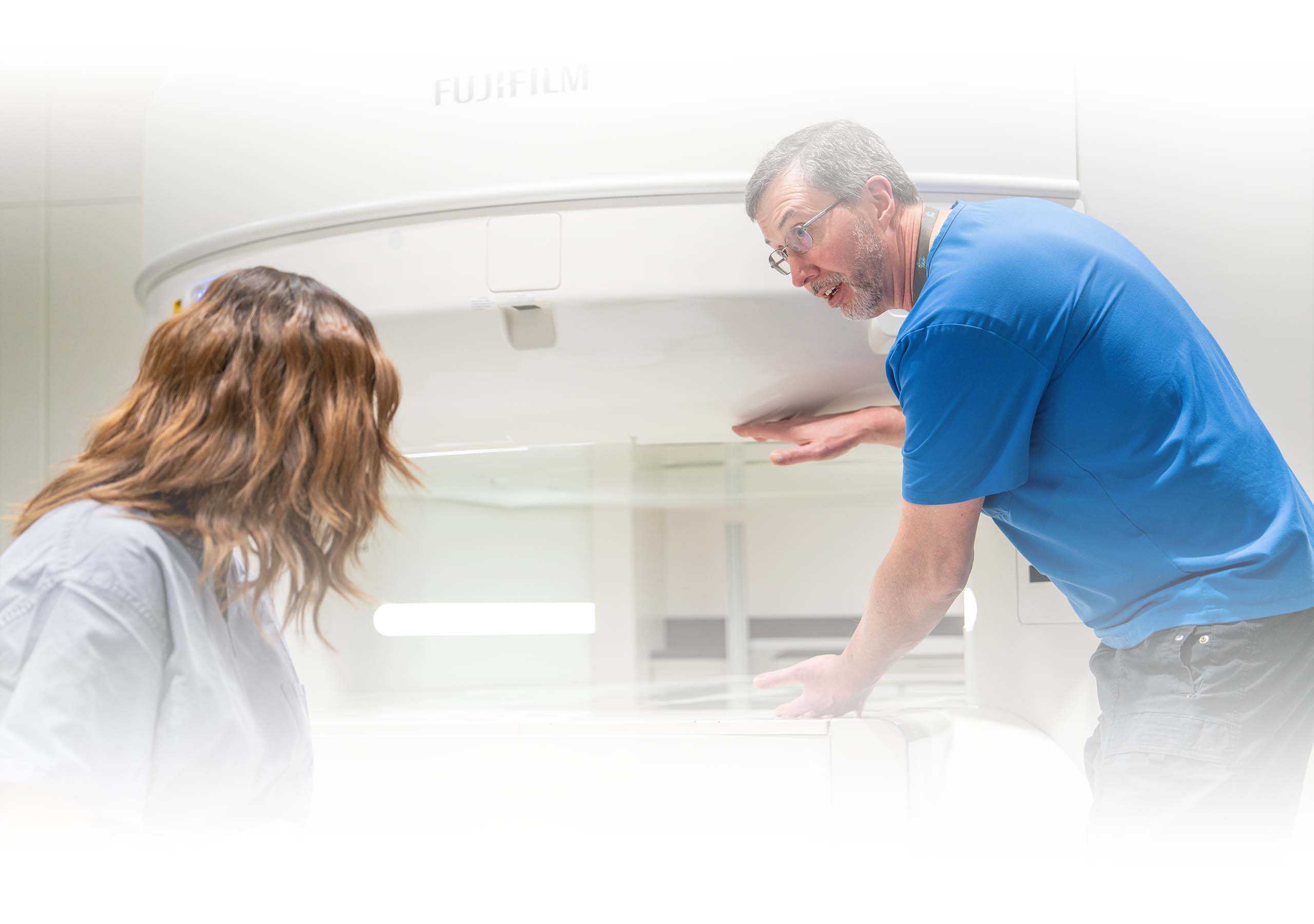 A technical explains the open MRI machine to a patient