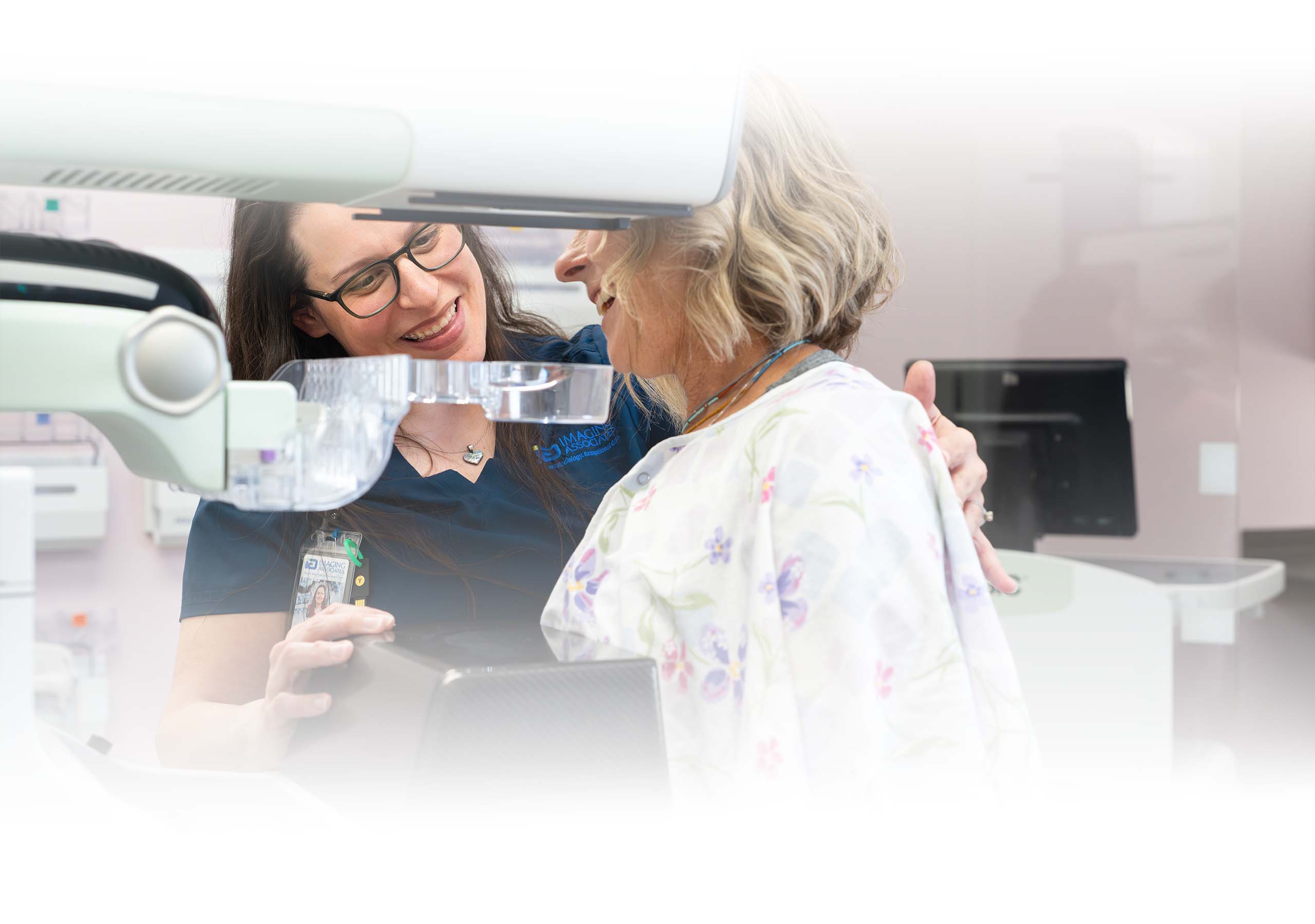 A technician smiling with a patient who is being prepared for a mammogram
